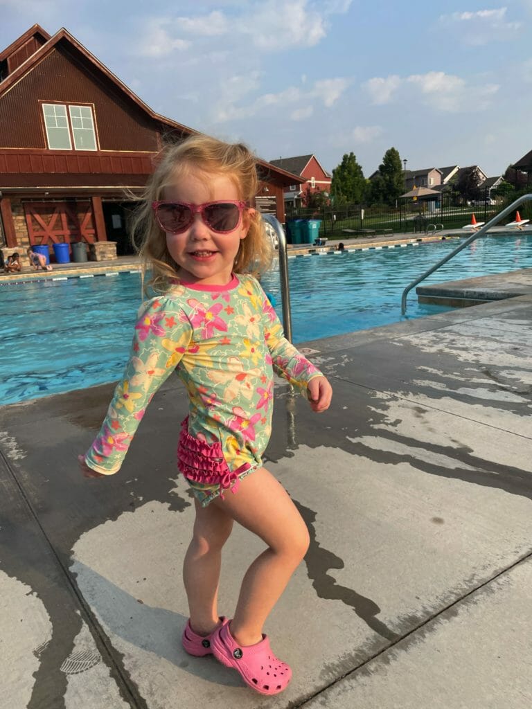 a girl in sunglasses standing in front of a pool