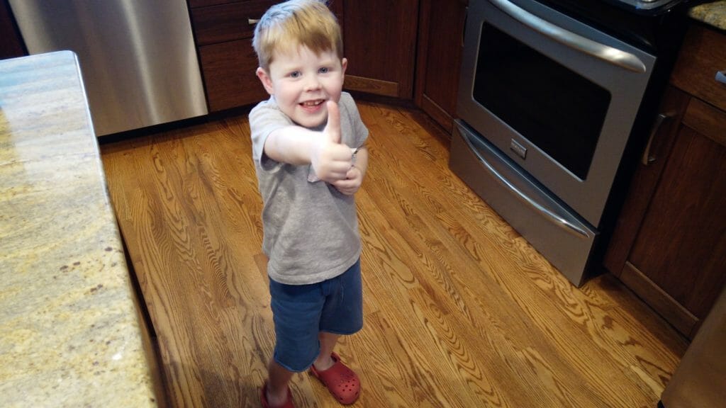 a boy standing in a kitchen giving a thumbs up